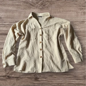 Beige skjorta med knappar  - Säljer en beige skjorta från SHEIN i storlek XL. Skjortan har lång ärm, knappar framtill och två bröstfickor. Materialet är strukturerat och känns mjukt mot huden. Perfekt för en avslappnad och stilren look.