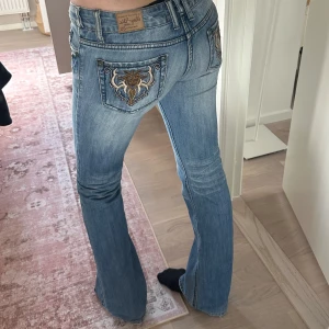 bootcut jeans med broderade bakfickor  - Säljer ett par ljusblå jeans från 2000-talet som har broderingar och nitar vid fickorna fram. Modellen har bootcut och normal passform. Perfekta för dig som gillar unika detaljer på jeansen. Storlek 34-36. Jag är 176. 🩷