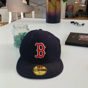 Baseballkeps  - Säljer en mörkblå keps från New Era, modell 59FIFTY, med Boston Red Sox-logga i rött och vitt framtill. Klassisk basebollkeps med platt skärm och broderad MLB-logga bak. Perfekt för dig som gillar sportig stil.