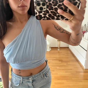 Ljusblå one shoulder topp från SHEIN - Säljer en ljusblå croppad topp från SHEIN med one shoulder-design. Toppen är i mjuk polyester med draperad effekt och bred resår nedtill. Perfekt för dig som vill ha en trendig och stilren look.