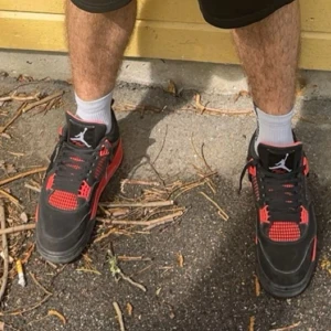 Nike Air Jordan 4 Retro Red Thunder - Säljer ett par Nike Air Jordan 4 Retro Red Thunder med svart ovandel i skinn och syntet, röda detaljer och meshpaneler. Ikonisk siluett med snörning och platt sula. Perfekta för dig som vill sticka ut med klassiska sneakers.