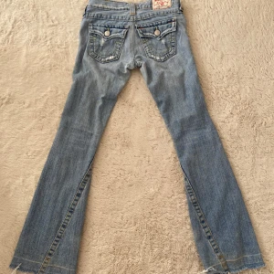 True Religion jeans - Säljer ett par lågmidjade ljusblå bootcut jeans från True Religion med slitningar framtill. rakt över midjan 35 cm innerbensläng 80 cm