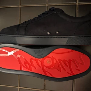 Mörkblå Christian Louboutin skor - Säljer ett par mörkblå sneakers från Christian Louboutin med klassisk röd sula och diskreta metalldetaljer på sidan. 