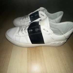Valentino Garavani sneakers - Snygga Valentino Garavani sneakers i vitt med en bred svart rem över snörningen. Skorna har en stilren design med Valention-logga på plösen. Perfekta för en trendig look. Lådan följer med. Pris kan diskuteras!!