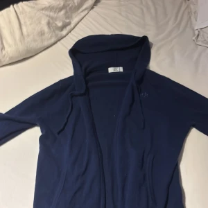 Mörkblå hoodie med dragkedja från Bvaldi  - Säljer en mörkblå hoodie från Bvaldi med dragkedja framtill och huva. Tröjan har långa ärmar och en enkel, stilren design. Perfekt för en avslappnad look. Storlek S