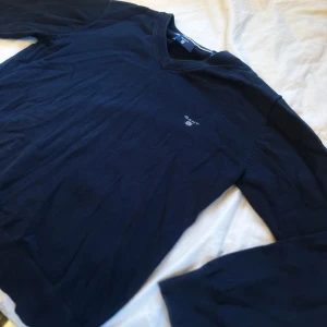 Mörkblå tröja från GANT - Säljer en klassisk mörkblå tröja från GANT med logga broderad på bröstet. Tröjan har långa ärmar och ribbade muddar vid hals, ärmslut och nederkant. Perfekt för en stilren och tidlös look. Tröjan är i storlek 15 years/ 170. Tröjan är i fint skick (se bilder). Hör gärna av dig vid frågor! MVH Axel 