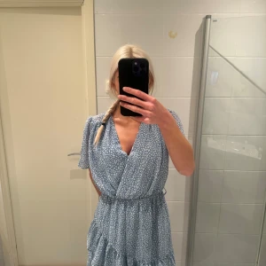 Ljusblå omlottklänning med volang - Säljer en söt ljusblå omlottklänning med volanger. Den är från Chelsea och helt oanvänd. Storlek S. Saknar banden i midjan.