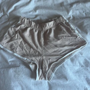 Beige sportiga shorts med vit kant - Säljer ett par beige shorts med vit kant och elastisk midja. De har en sportig look och är perfekta för varma dagar eller träning. Materialet känns mjukt och lätt, vilket gör dem riktigt bekväma att ha på sig.