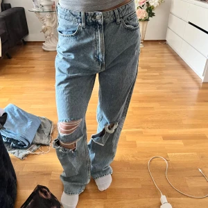 Ljusblå loose fit jeans med hål - Säljer ett par ljusblå jeans från &Denim med loose straight passform och hög midja. Byxorna har slitna detaljer och stora hål vid knäna för en trendig look. Perfekta för dig som gillar en avslappnad stil.