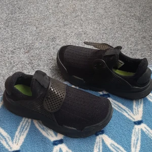 Svarta Nike sneakers med mesh och kardborre - Säljer ett par svarta Nike  sneakers med ventilerande mesh-ovandel och bred kardborreknäppning. Skorna har rund tå, platt sula och detaljer i syntetmaterial. Perfekta för dig som vill ha en sportig och bekväm stil. Skor är mycket lätta och bekväma i mycket bra skick. 