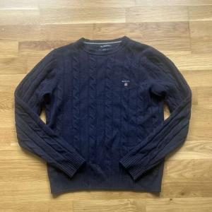 Kabelstickad gant tröja  - Säljer en mörkblå kabelstickad tröja från GANT i 100% lammull. Tröjan har rund halsringning, långa ärmar och ett broderat GANT-emblem på bröstet. Klassisk och stilren modell som passar perfekt till kyligare dagar.
