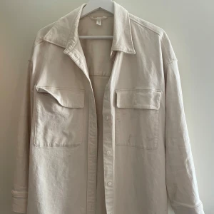 Beige jeansjacka med stora fickor - Säljer en stilren beige jeansjacka med två stora bröstfickor och klassisk krage. Skjortan har långa ärmar och knäppning framtill. Den har en fläck men den går bort innan jag skickar i väg den. 