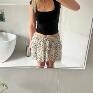 Vit kortkjol med svart mönster - Säljer en krämvit kort kjol med volang och resår i midjan. Den var tidigare högmidjad men har klippt och vikt ner kanten för en snyggare passform. Från Lindex i storlek S. Använd men i bra skick. 