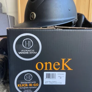 Svart ridhjälm OneK Avance Wide Brim - Snygg svart ridhjälm från OneK med bred skärm (Wide Brim) och matt finish. Hjälmen har en stilren design och är utrustad med KLICK-N-GO solglasögonssystem. Perfekt för ridning och ger extra skydd mot solen.