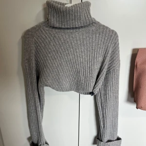 Grå croppad polotröja - Säljer en grå croppad polotröja med ribbat material och långa ärmar. Perfekt för lager-på-lager och ger en trendig look