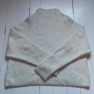 Vit stickad tröja från Kappahl - Mysig vit stickad tröja från Kappahl med hög hals och lång ärm. Tröjan har en enkel och stilren design med ribbad struktur, perfekt för lager-på-lager och kalla dagar.