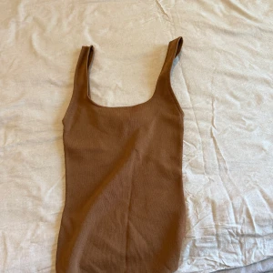 Brun ribbad ärmlös klänning - Säljer en brun ribbad klänning med ärmlös design och fyrkantig ringning. Klänningen har en tight passform och är perfekt för dig som gillar en enkel men stilren look.