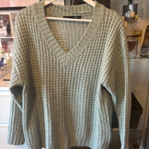 Ljusgrön stickad tröja med v-ringning från Lager 157 - Mysig ljusgrön stickad tröja från 157 med djup v-ringning och grovstickat mönster. Tröjan har långa ärmar och breda ribbade muddar vid hals, ärmslut och nederkant. Perfekt för lager-på-lager under kyliga dagar. Tyvärr ser den mer gul ut på bilden än i verklighet.