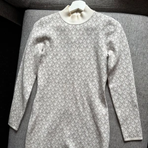 Vit mönstrad långärmad klänning - Säljer en vit långärmad klänning med diskret grått mönster och hög krage. Klänningen har en kroppsnära passform och är perfekt för dig som gillar stilrena och enkla plagg med en twist.