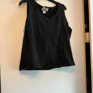 Svart linnetopp från ODC - En enkel svart linnetopp från ODC i mjuk bomullsblandning med lite stretch. Toppen är ärmlös och har en klassisk rund halsringning. Perfekt att matcha med kjol eller jeans för en avslappnad look. Skulle säga att storleken är S-M