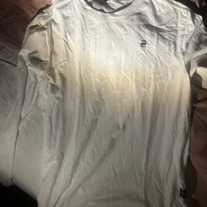 Vit långärmad t-shirt från G-Star RAW - Säljer en stilren vit långärmad äkta t-shirt från G-Star RAW. Den har en liten logga på bröstet och är tillverkad i ett mjukt material. Perfekt för en avslappnad look.