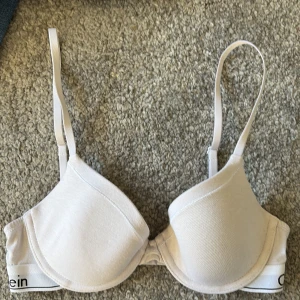 Vit bh från Calvin Klein - Säljer en stilren vit bh från Calvin Klein med justerbara axelband och klassisk logga på bandet. Aldrig använd, endast provad. Storlek står ej, men tippar på 70B.