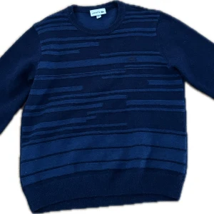 Mörkblå tröja från Lacoste - Säljer en stilren mörkblå tröja från Lacoste med diskreta ränder. Tröjan har långa ärmar och en klassisk rund halsringning. Perfekt för en avslappnad men ändå elegant look.