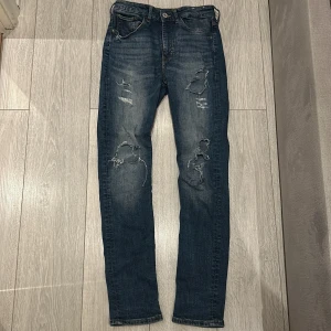  slim jeans - Blå - Snygga blå jeans med slitningar och en klassisk femficksdesign. De har en dragkedja och knapp framtill. Perfekta för en avslappnad stil.
