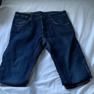Mörkblå jeans från Dondup  - Säljer ett par mörkblå jeans  från Dondup  med tapered fit. Byxorna har klassisk femficksdesign och en snygg detalj med broderad logga på baksidan. Perfekta för en avslappnad stil. Storlek 34 men sitter som 33 eftersom de är ganska tajta. Nypris 3199 mitt pris 699. Uppen för bud. 