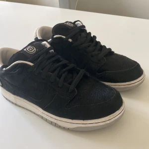 Svart vita Nike SB Dunks Low medicom you  - Snygga svarta sneakers med vit sula och snörning. Skorna har en unik textur och en vit detalj på hälen. Perfekta för en stilren look. Det är en collabration.  Har box samt kvitto. 