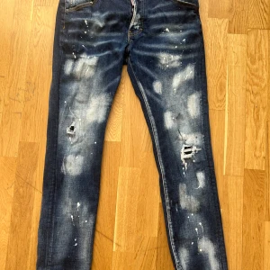 Mörkblå jeans från Dsquared2 - Snygga mörkblå jeans från Dsquared2 med slitna detaljer och färgstänk för en cool look. Jeansen har en klassisk femficksdesign och en bekväm passform. Perfekta för dig som vill ha en unik stil (storlek 52). 