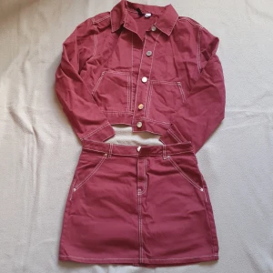 Set med vinröd kjol med matchande jacka från H&M  - Matchande set med vinröd kjol i kort modell från H&M med matchande jacka. Kjolen har en dragkedja och knappar framtill samt praktiska fickor. Jackan har två fickor fram och kontrasterande sömmar. Så snyggt set men kommer tyvärr inte till använding hos mig ❤️ material 100% bomull. 