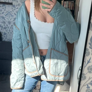 Ljusblå quiltad jacka - Säljer en ljusblå quiltad jacka med bruna kantdetaljer och knappar. Jackan har en avslappnad passform och stora fickor framtill. Perfekt för en stilren look. Storlek xs men väldigt oversist 