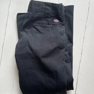 Svarta byxor från Dickies - Snygga svarta byxor från Dickies i modellen Slim Straight. Perfekta för en stilren look med en bekväm passform. Byxorna har en klassisk design med fickor och en diskret logga på baksidan. W30 L30