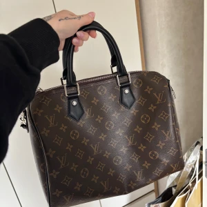 Monogram Väska 30cm - Jättefin väska, i monogram och svarta/silver detaljer. Använd en gång, storlek 30 (dvs 30cm) kommer med dustbag, lås och nyckel samt ett axelband (se bild) 