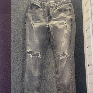 Grå jeans från Good American - Säljer ett par grå jeans från Good American med slitna detaljer och en avslappnad look. De har en klassisk femficksdesign och är perfekta för en trendig stil. Passar bra till sneakers eller boots.