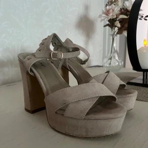 Beige klackar - Snygga beige sandaler med hög klack och öppen tå. De har en justerbar rem med spänne och dekorativa nitar på sidan. Perfekta för balen