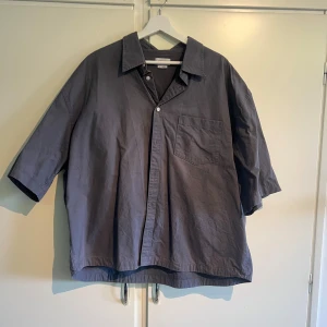 Grå/blå skjorta från Weekday - Säljer en stilren grå/blå skjorta från Weekday i storlek XL. Skjortan har en klassisk krage, korta ärmar och en bröstficka. Perfekt för en avslappnad look.