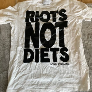 Vit t-shirt från Dondup - Snygg vit t-shirt från Dondup med det djärva trycket 'RIOTS NOT DIETS' i svart på framsidan. Perfekt för att göra ett statement. Tillverkad i Italien.