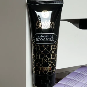 Golden Sparkle Exfoliating Body Scrub - Golden Sparkle Exfoliating Body Scrub från Sence i en elegant svart tub med guldmönster. Innehåller 150 ml och är designad för att ge huden en mjuk och len känsla. Perfekt för att fräscha upp huden med en lyxig känsla. Använd en gång