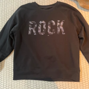 Svart tröja med texten ROCK från Zadig Voltaire  - Säljer en svart tröja med texten ROCK i glittriga bokstäver på framsidan. Tröjan har långa ärmar och en rund halsringning. Perfekt för en avslappnad stil med lite edge.