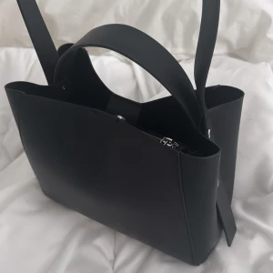 Svart axelväska - Snygg svart axelväska i skinn med stilren design. Köpt på gina, använd max 2 gånger. Jättefin väska som ser helt ny ut. Säljer pga att jag är i behov av större väska. Nypris 400kr