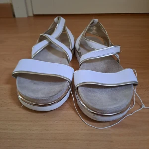 Vita sandaler med remmar - Snygga vita sandaler med korsade remmar och en justerbar spänne. De har en platt sula och en öppen tå-design, perfekt för varma dagar.