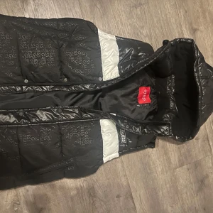 Svart dunväst från Guess - Svart vit grues väst med universum bokstäver i de svarta, nypris 1700 använd 1-3 gånger köptes ny 