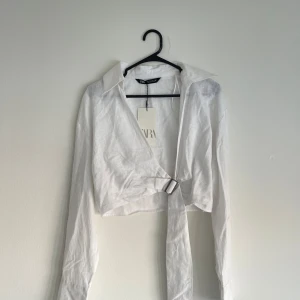 Vit croppad linneskjorta från Zara - Helt oanvänd croppad linneskjorta med knytning. Perfekt till sommaren som t.ex. bikini cover up. Ordinarie pris 220kr