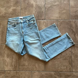 Ljusblå jeans med slits - Snygga ljusblå jeans med en klassisk femficksdesign och en liten slits vid bensluten. Perfekta för en avslappnad stil. De har en rak passform och är tillverkade i 99% bomull och 1% elastan. Midjemått:36cm, innerbensmått: 79cm