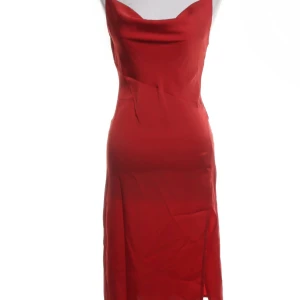 Röd axelbandslös klänning - Snygg röd klänning med smala axelband och en elegant slits. Perfekt för festliga tillfällen. Klänningen har en figurnära passform och är tillverkad i ett glansigt material som ger en lyxig känsla.