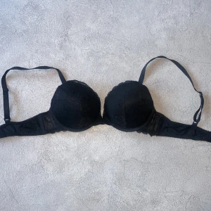Svart spets-bh med push upp  - Snygg svart bh med push upp, spetsdetaljer och justerbara axelband. Perfekt för en elegant look. Den har en klassisk design med en bekväm passform.