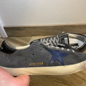 Golden Goose skor - Snygga grå sneakers från Golden Goose med en blå stjärna på sidan och GGDB-märke. Skorna är använda men i väldigt bra skick. Priset går att diskutera vid snabb affär.