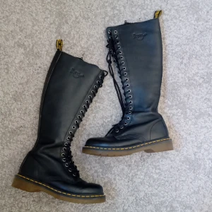 Svarta höga boots från Dr. Martens - Säljer ett par svarta höga boots i läder från Dr. Martens med snörning och dragkedja. De har den klassiska gula sömmen och en robust sula. Perfekta för en edgy look! De är använda ett fåtal gånger därav är de lite skrynkliga nere vid fotleden. Säljer då de inte kommer till användning. Priset kan diskuteras💞💞